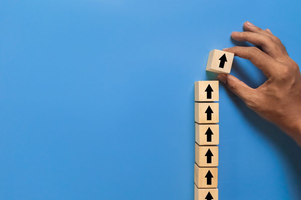male hand put arrow up stack on wooden blocks isolated on blue background