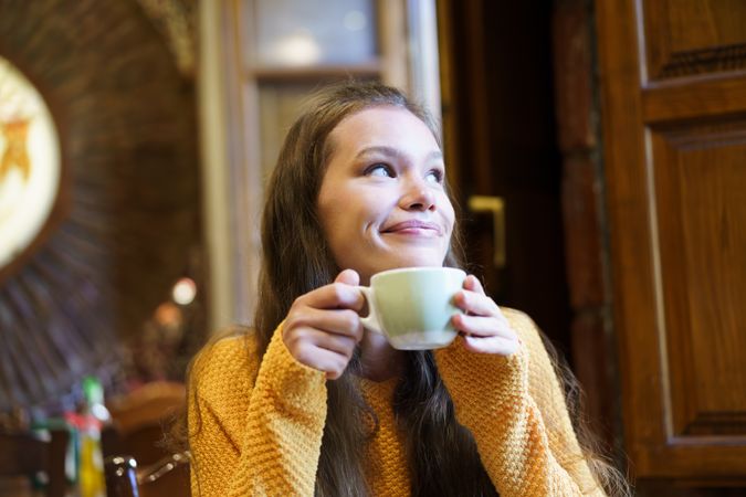 A Young Woman Enjoys a Warm Cup of Coffee in a Cozy Cafe, Embracing Comfort and Joy