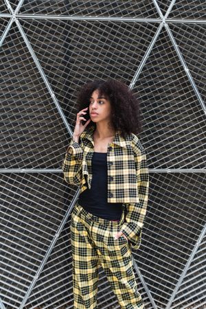 Trendy Black woman talking on smartphone against grid fence
