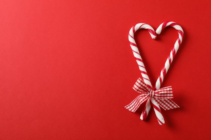 Sweet candy canes with bow on red background, space for text