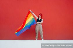 Young woman holding rainbow flag standing against red background 4OqAj0