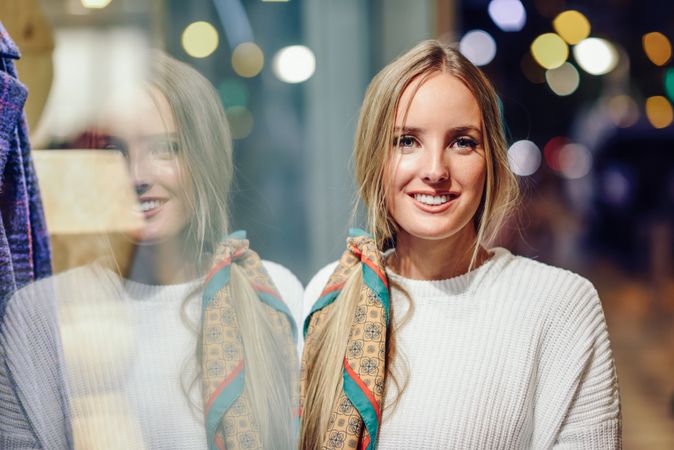 Smiling woman standing next to shop window at night