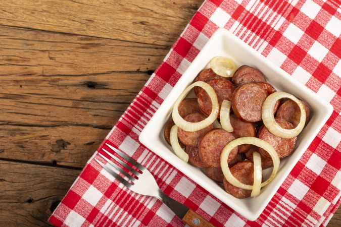 Sliced calabrese sausage with onion on wooden background.