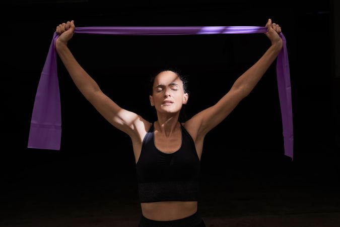 Sportswoman exercising with elastic band in dark room