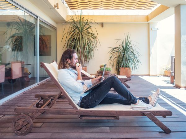 male browsing laptop and enjoying apple on lounge in flat