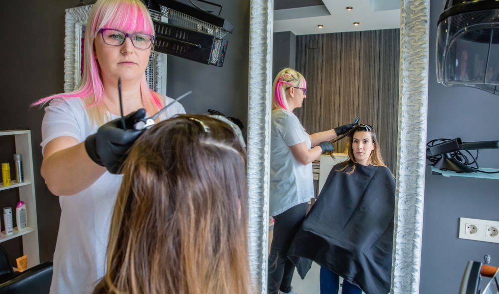 Hair dresser with pink hair coloring client's hair in salon