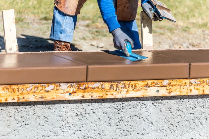 Construction Worker Using Trowel On Wet Cement Forming Coping Around New Pool