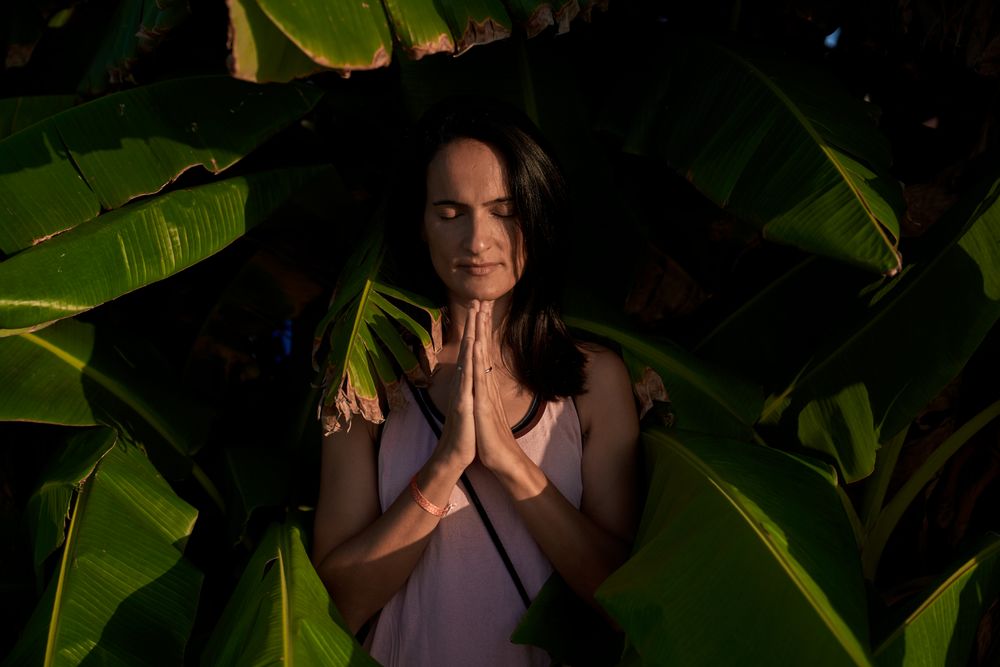 Peaceful Hispanic woman with prayer hands near green trees