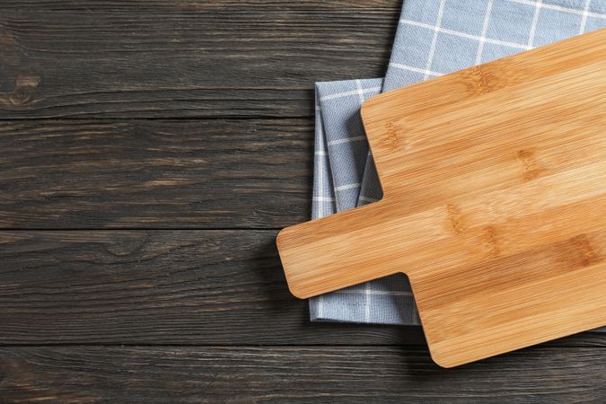 Cutting board with kitchen towel on wooden background, space for text
