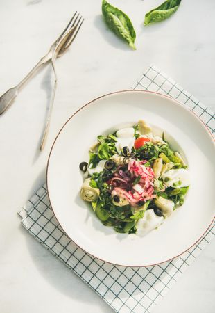 Artichoke salad in bowl, light background with checkered napkin, vertical composition