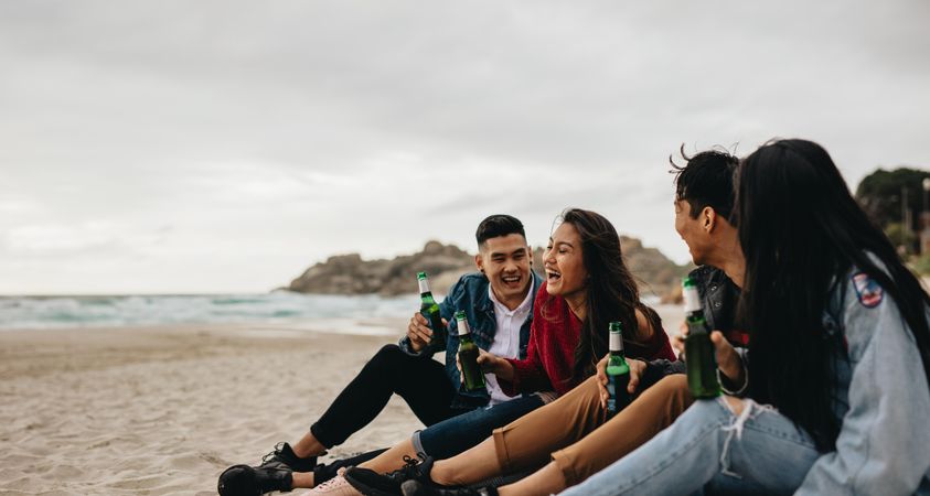Group of men and women sitting at the sea shore with beers