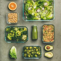 Variety of vegetable dishes in glass containers with bottles of dressing, square crop