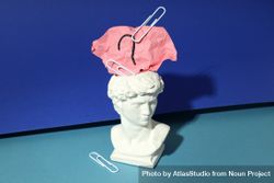 Marble bust of David with crumpled pink post it note with question mark and paper clips, on blue 4mr7Wb