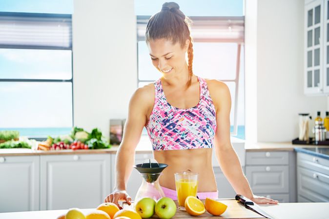 Fit woman in kitchen looking down at cutting board with juice and fresh fruit