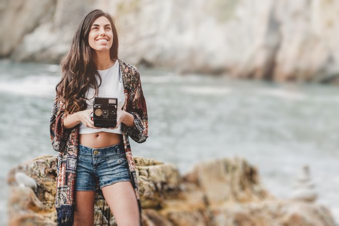 Woman with camera on shore near stones and water