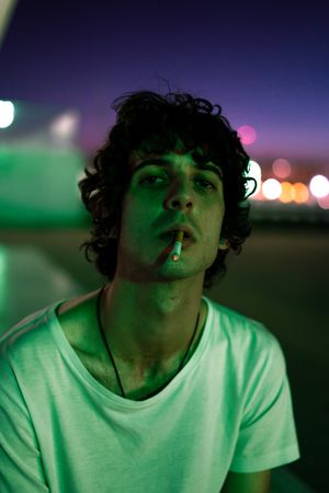 Adult man smoking while looking at camera during sunset