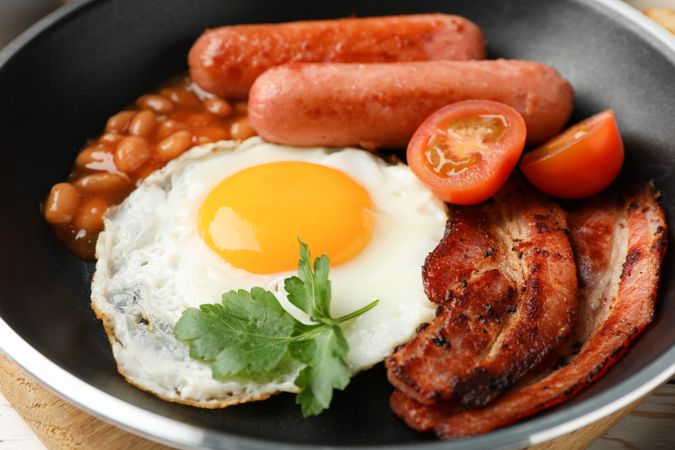 Top view of eggs, sausages and tomatoes cooking in pan