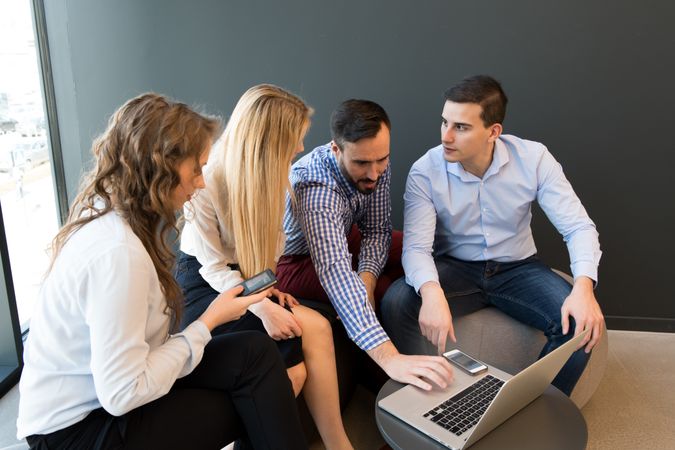 Stylish coworkers gathering around laptop in office