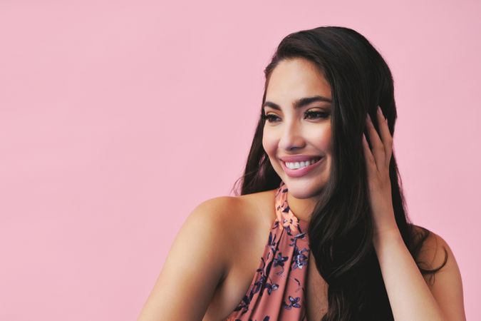 Smiling Hispanic woman with one hand up to her head in pink room