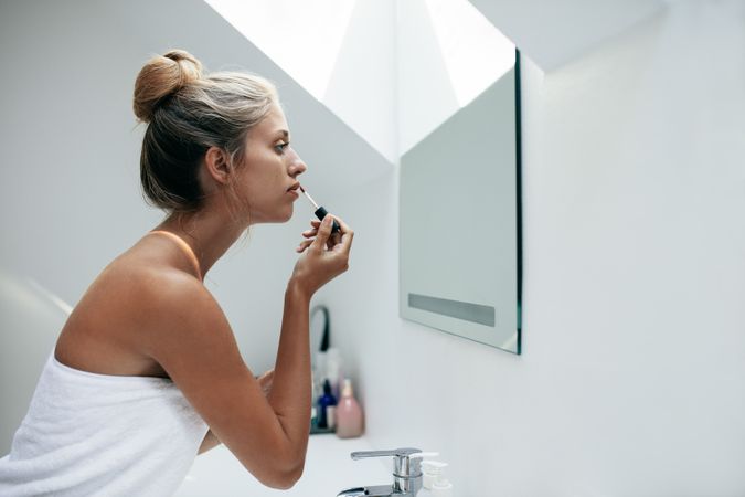 Side view shot of woman applying lip gloss in bathroom