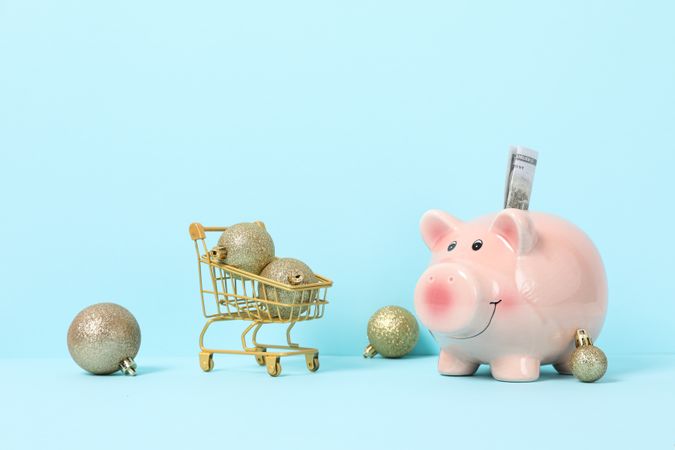 Piggy bank and New Year's balls in trolley on blue background, space for text