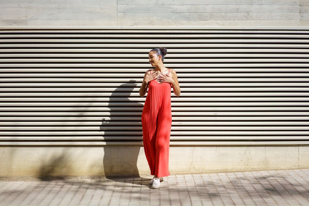 A Stylish Woman Dressed in a Vibrant Red Dress Posing in Front of a Textured Wall