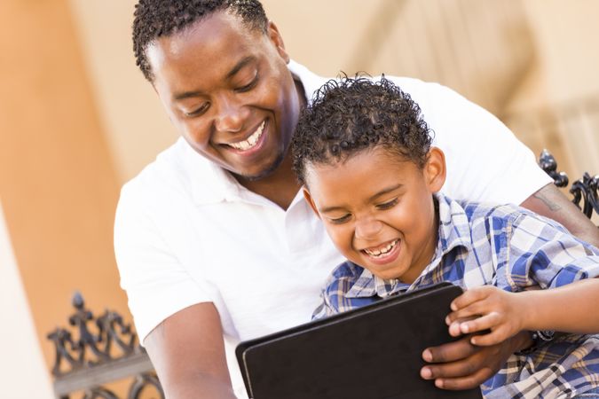 Smiling Black Father and Son Using Tablet On Balcony