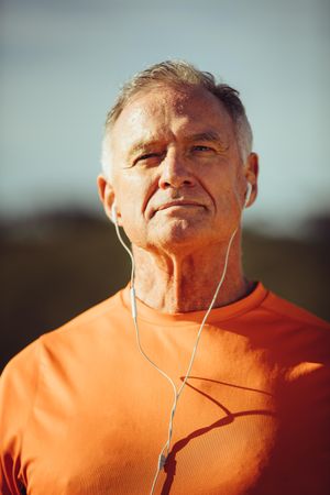 Portrait of a man standing outdoors on a sunny day listening to music