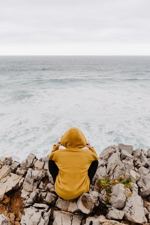 Person in yellow hoodie on stony shore