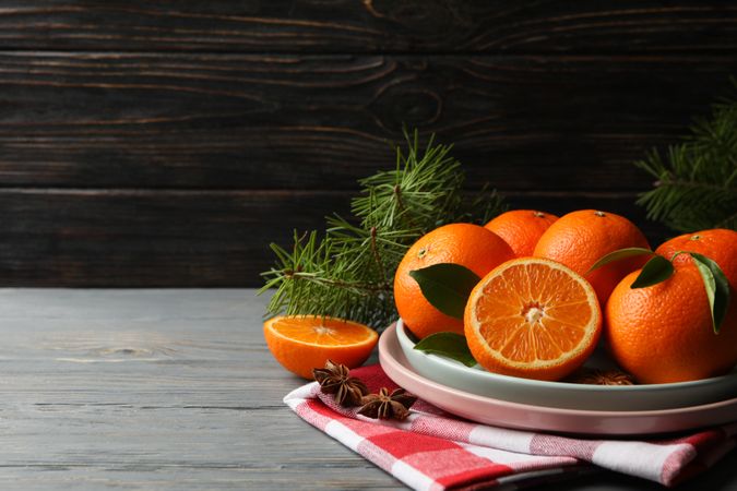 Plates with mandarins, pine branches, napkin and cinnamon on wooden background