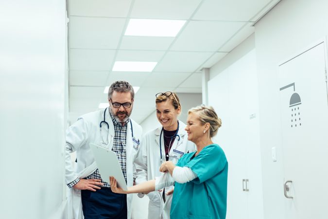 Mature female nurse showing clipboard to doctors in hallway