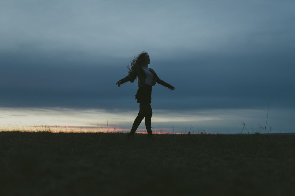 Young woman with long hair spinning in a field at dusk