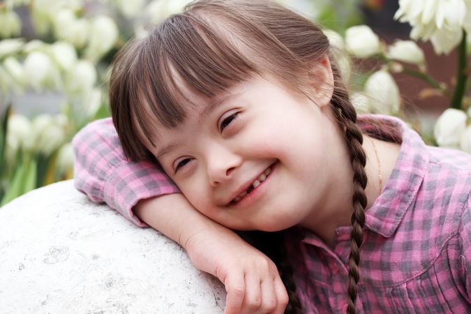 Portrait of smiling young girl with Down syndrome leaning on a rock
