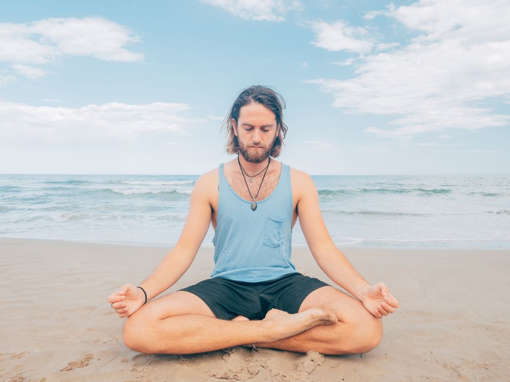 Man training yoga on beach