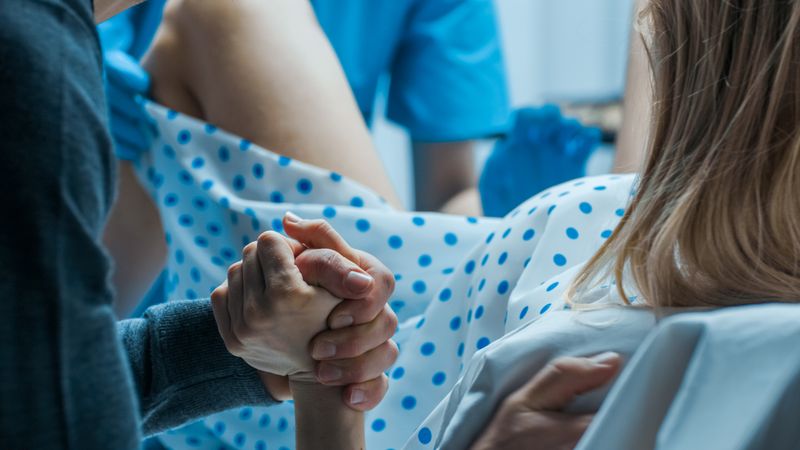 Emergency In the Hospital: Woman Giving Birth, Husband Holds Her Hand in Support, Obstetricians Assisting