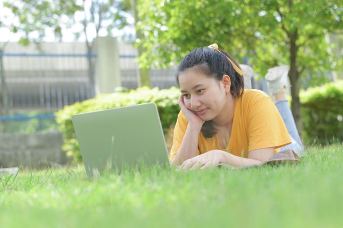 A young woman lying on the lawn at home using a laptop.