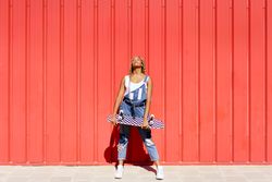 Woman leaning against red wall with skateboard