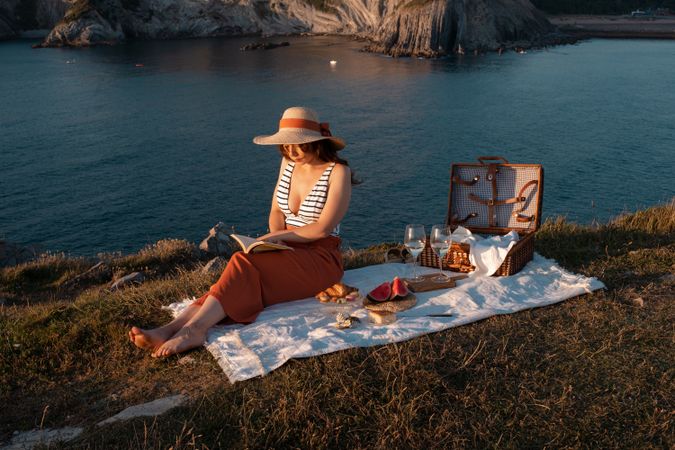 Woman reading on mat for picnic on seashore