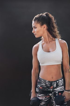 Female fitness woman with dumbbells on dark background