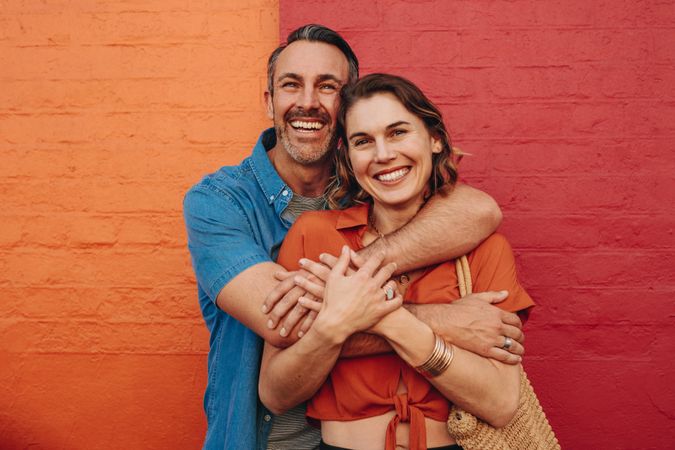 Happy couple embracing in front of a bold red and orange wall