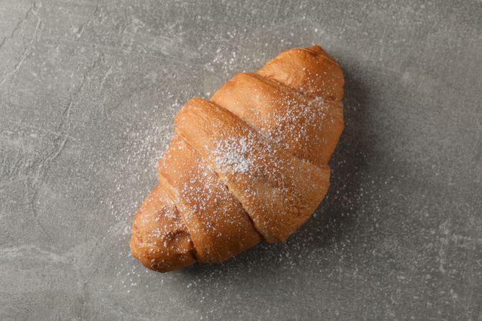 Croissant with powdered sugar on grey background, top view
