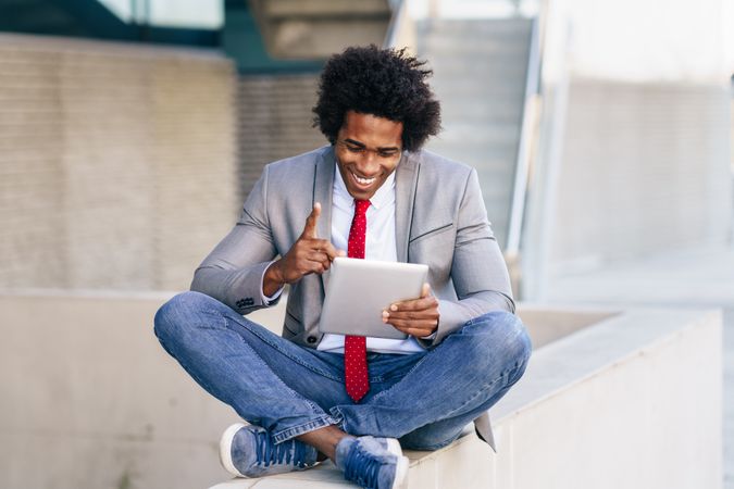 Happy man looking down at his digital tablet sitting cross legged