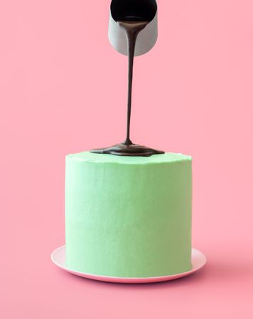 Pouring melted chocolate over peppermint cake, isolated on a pink background