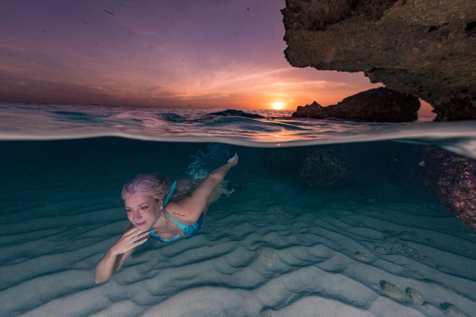 Blond fairytale female mermaid swimming along sea bottom