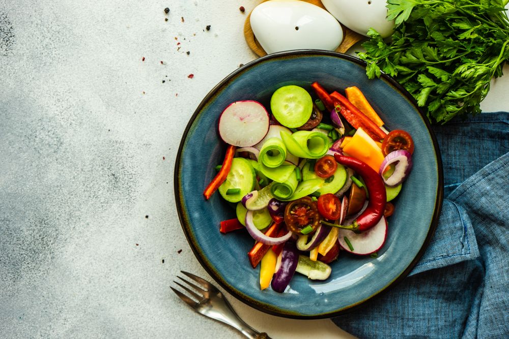 Top view of raw salad with chopped vegetables served with garnish on blue plate