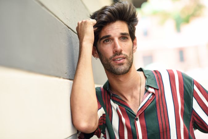 Portrait of calm man with dark hair leaning on wall outside