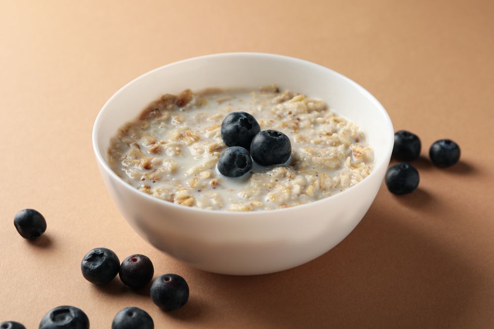 Bowl with oatmeal porridge and berry on craft background, close up