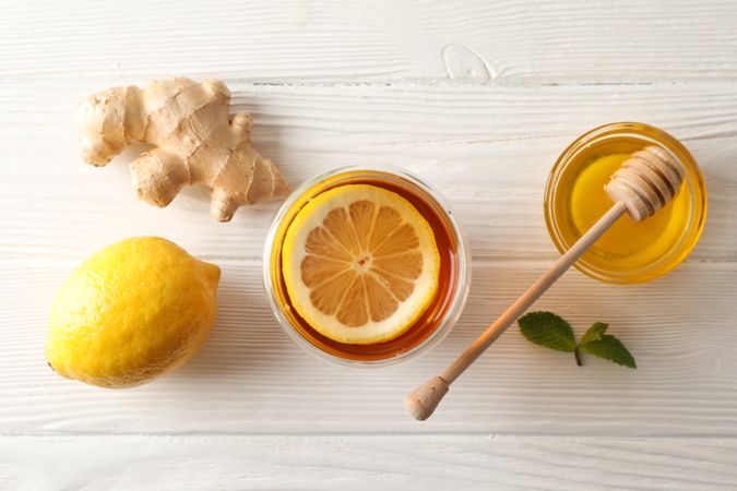 Glass of tea with lemon, mint, honey, dipper and ginger on wooden background, top view