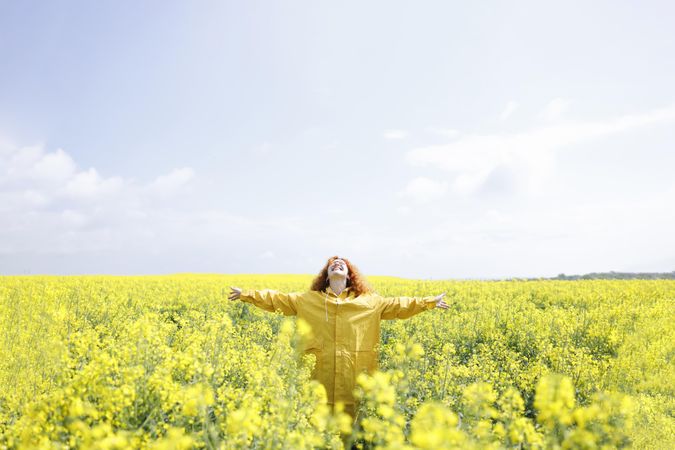 Woman in yellow coat with arms outstretched in yellow field