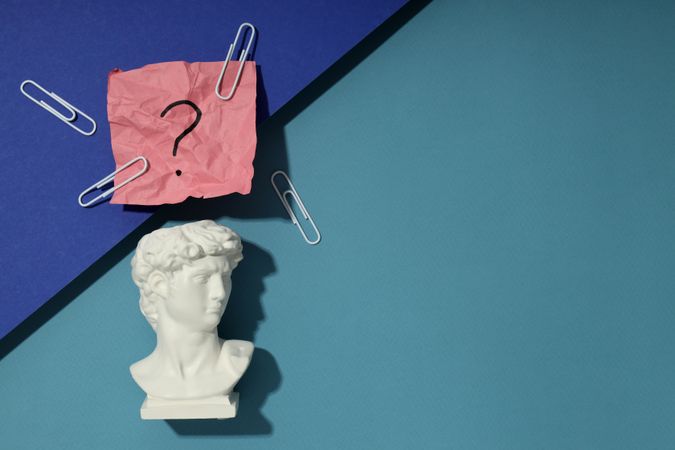 Marble bust of David with crumpled pink post it note with question mark and paper clips, copy space